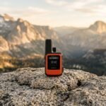 Garmin inReach Mini 2 satellite communicator resting on a rock in a remote mountainous landscape.