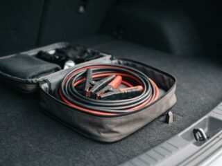 Jumper cables coiled inside a vehicle trunk emergency kit.