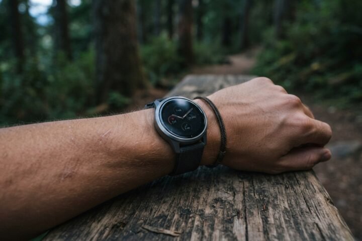 A person wearing a modern GPS smartwatch on their wrist while resting at a trail bench during twilight.