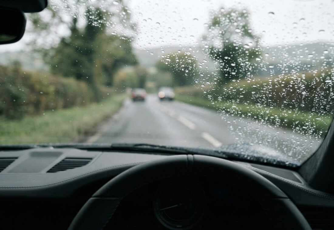 Close-up view through a vehicle windshield during light rain with soft focus on the road ahead.