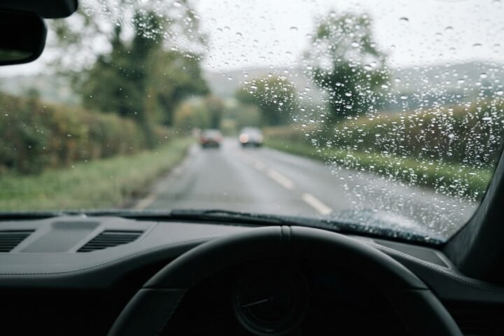 Close-up view through a vehicle windshield during light rain with soft focus on the road ahead.